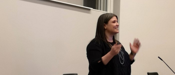 photo of a white woman with dark long hair in a black blouse gesticulating while speaking