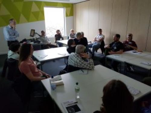 photo of teaching setting: a colourful room with an older audience gathered around white tables