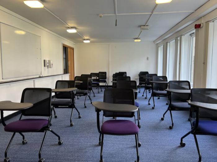 Flat floored teaching room with tablet chairs and whiteboard.