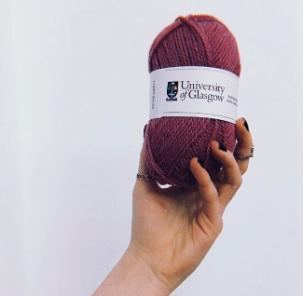 Hand holding a ball of University of Glasgow wool