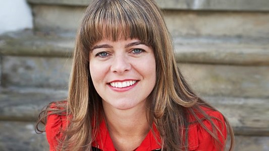 shot of a white woman with a brown fringe and long hair in front of grey stairs