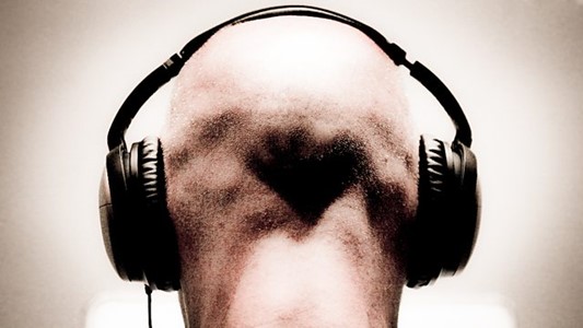 black-and-white photo of the back of a bald man's head with big black headphones