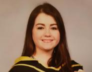 Emma Fletcher smiling to the camera in a set of graduation robes.