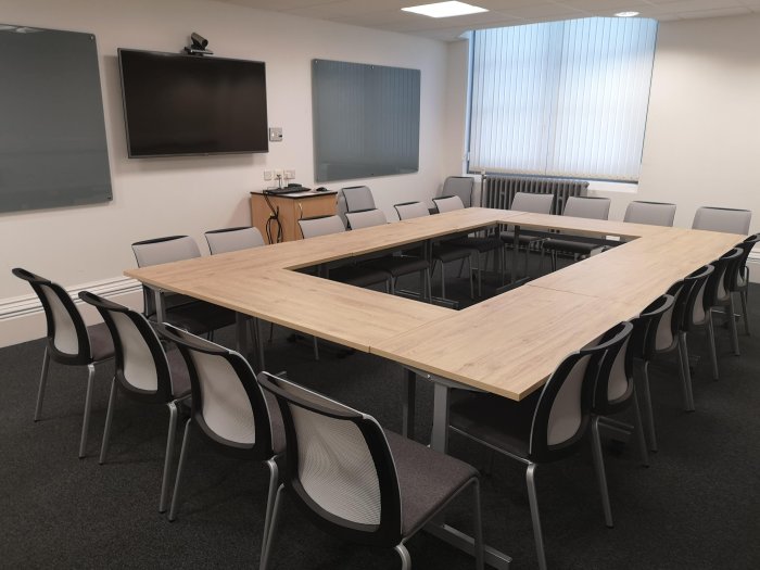 Flat floored meeting room with boardroom tables and chairs, glassboards, and video monitor
