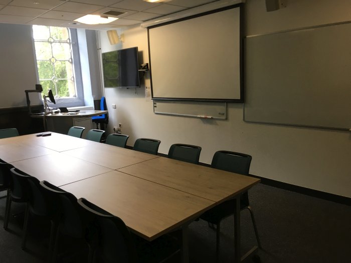 Flat floored meeting room with boardroom table and chairs, screen, whiteboards, video monitor, visualiser, and PC