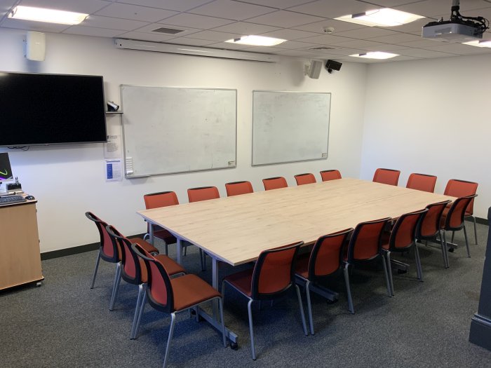 Flat floored meeting room with boardroom table and chairs, whiteboards and video monitor