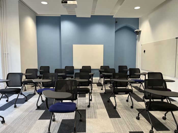 Flat floored teaching room with tables and chairs in horseshoe set-up and whiteboard
