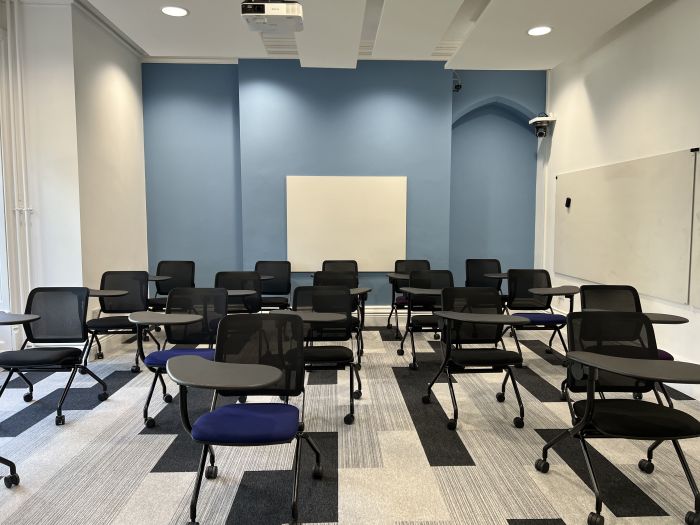 Flat floored teaching room with tablet chairs, whiteboard, and projector.