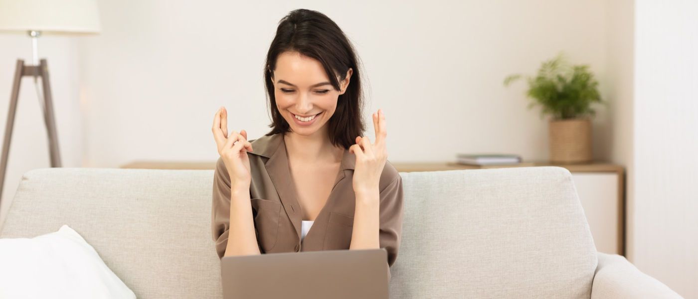 Woman looking at laptop with fingers crossed for luck