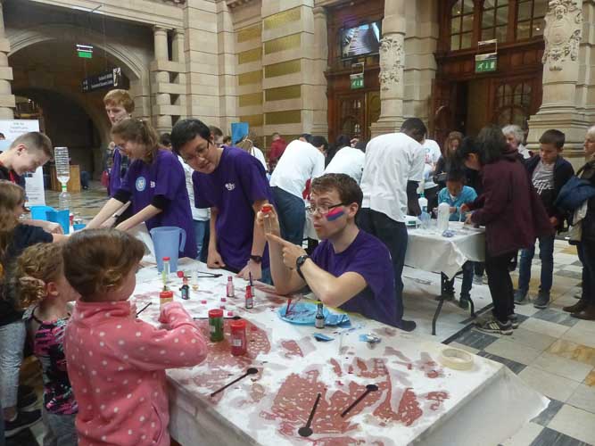 Photograph of three demonstrators with test tubes, food colouring and glitter. 