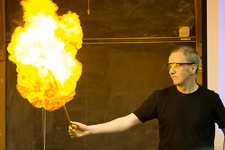 Photograph of a man holding a stick that is on fire. 