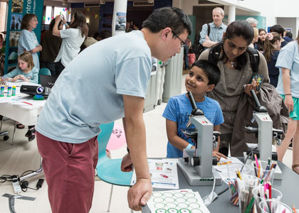 Photograph showing a GSF volunteer with a microscope teaching a child and his mother how it is operated. 