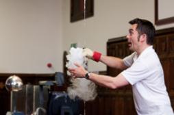 Photograph of a man demonstrating a chemical reaction involving white smoke. 