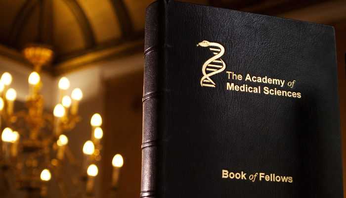 A copy of the Academy of Medical Sciences book of Fellows stood upright with a chandelier behind