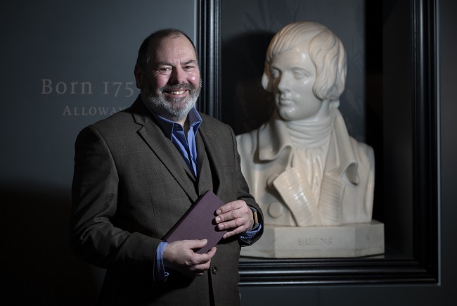 Professor Gerard Carruthers standing by a bust of Robert Burns. Photo Credit Martin Shields