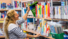 A student removing Axon Degeneration book from shelf in library