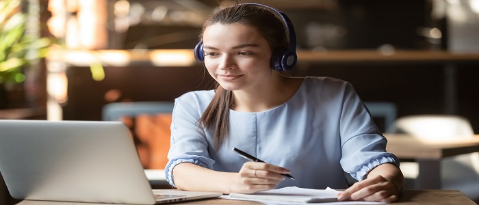 Picture of a woman working on a laptop wearing headphones