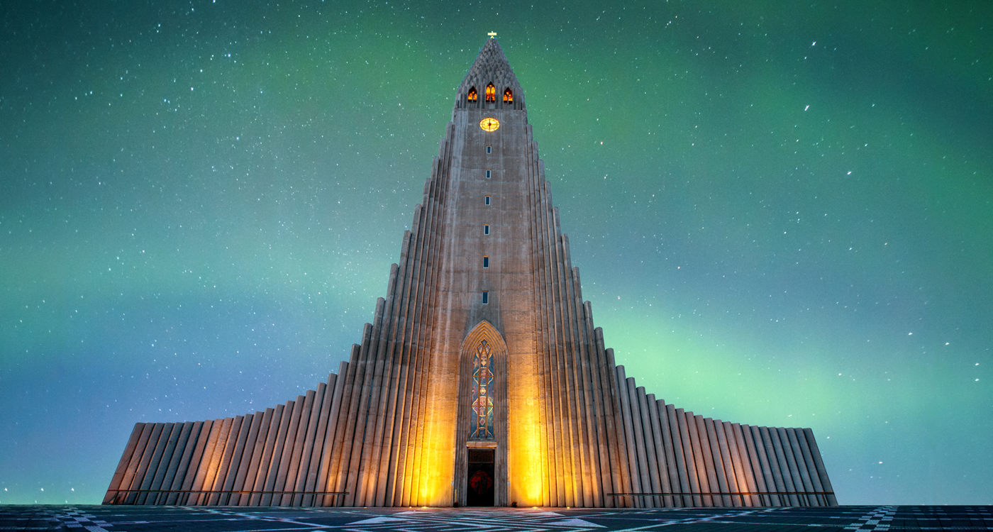 Exterior of the Hallgrímskirkja Church with a colourful aurora borealis in background.