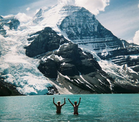 Student Moray Swanson standing in an ice blue lake below snowcapped mountain