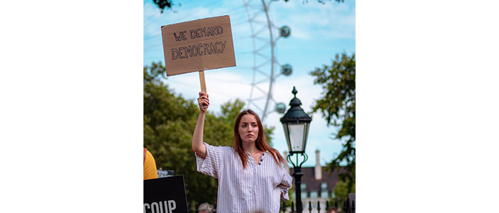 Photo of a woman holding a placard saying 'We demand democracy'