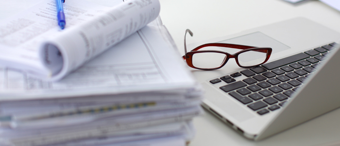 Photo of laptop, glasses and a pile of papers