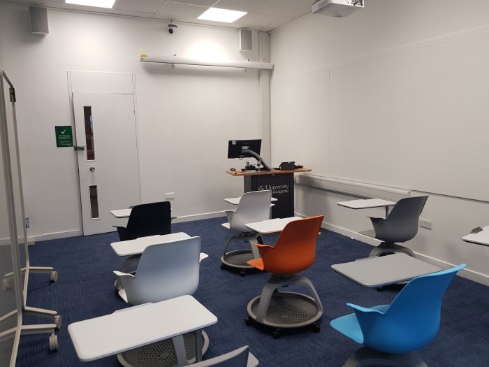 Flat floored teaching room with tablet chairs, whiteboard, screen and PC