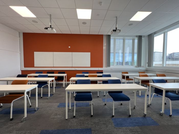 Flat floored teaching room with rows of tables and chairs, projectors, and whiteboards.