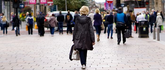 An image of a woman walking down pedestrianised city street towards traffic crossing