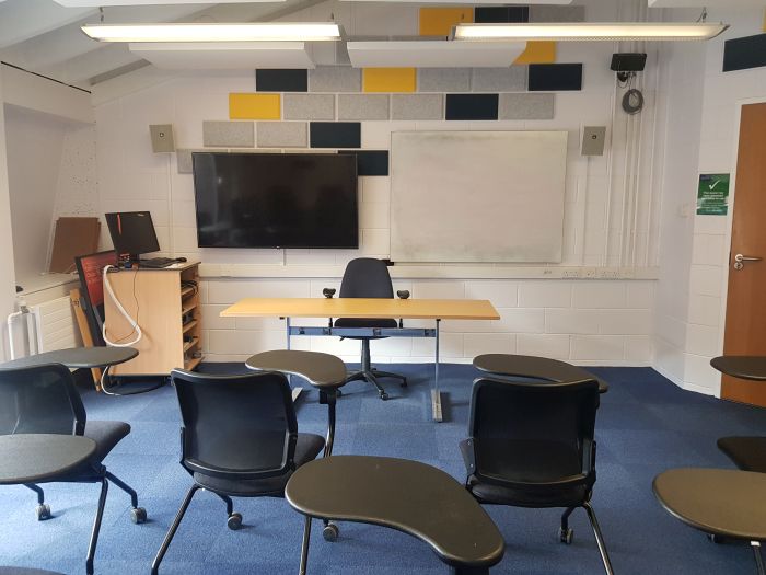 Flat floored teaching room with tables and chairs, whiteboard, video monitor, and PC