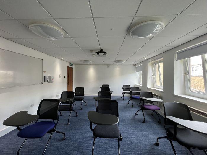 Flat floored teaching room with tablet chairs, whiteboard, and projector.