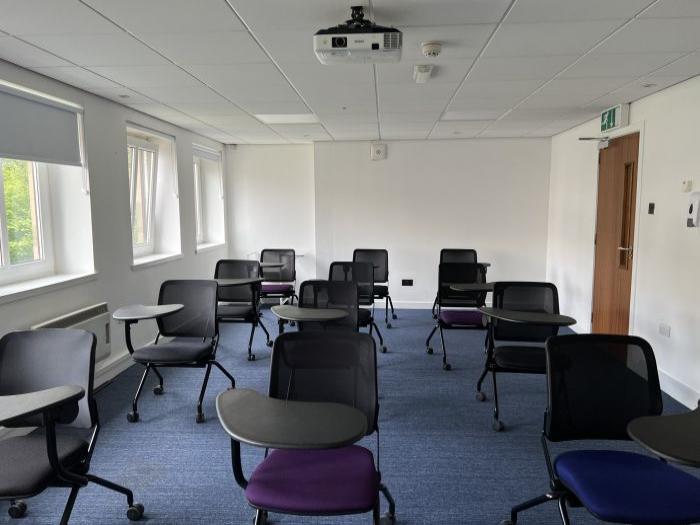 Flat floored teaching room with tablet chairs and projector.