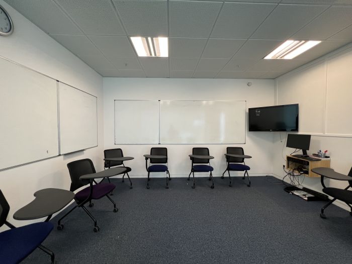 Flat floored teaching room with tablet chairs, whiteboards, video monitor, and PC.