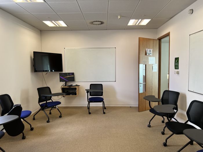 Flat floored teaching room with tablet chairs, whiteboard, video monitor, and PC.