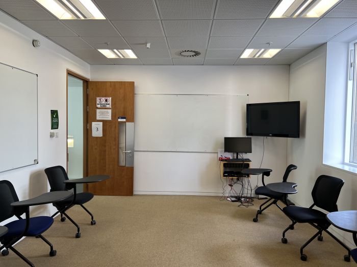 Flat floored teaching room with tablet chairs, whiteboards, video monitor, and PC.