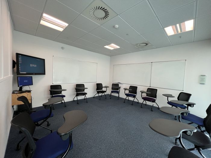 Flat floored teaching room with tables and chairs in round table set-up and whiteboards