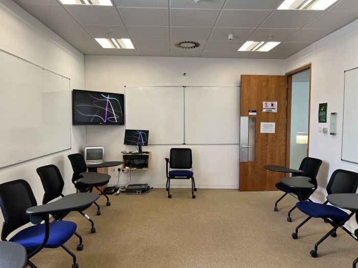 Flat floored teaching room with tablet chairs, whiteboards, video monitor, and PC.