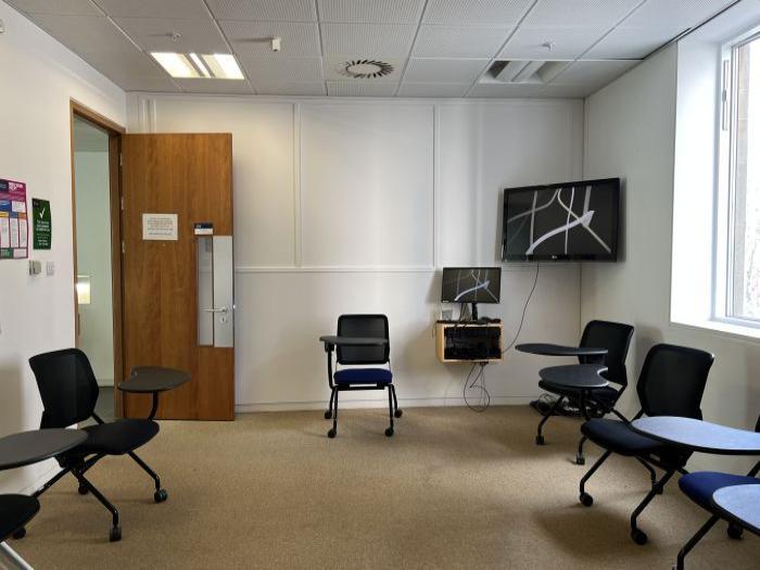 Flat floored teaching room with tablet chairs, video monitor, and PC.