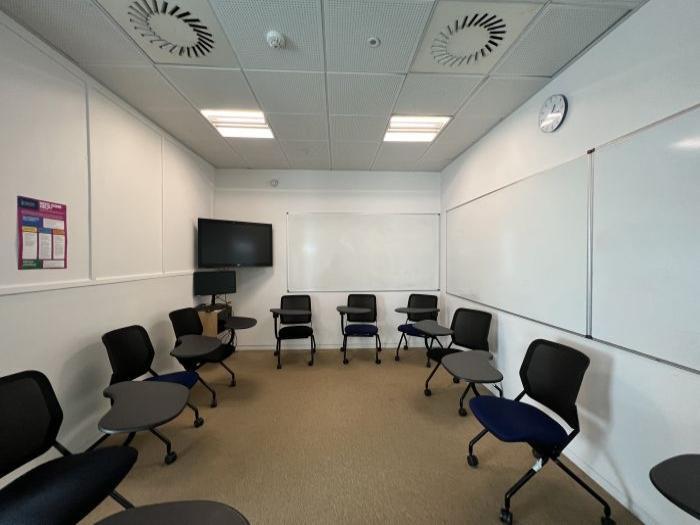 Flat floored teaching room with tablet chairs, whiteboards, video monitor, and PC.