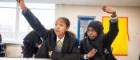 Two high school pupils raise their hands to answer a question in class. Photo courtesy of IntoUniversity