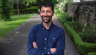 An image of Dr Daniel Streicker stood with arms folded, smiling in a lane with grass and trees behind him