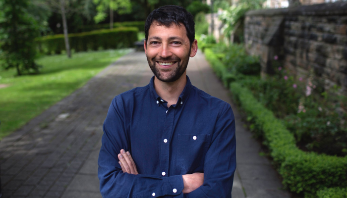 An image of Dr Daniel Streicker stood with arms folded, smiling in a lane with grass and trees behind him