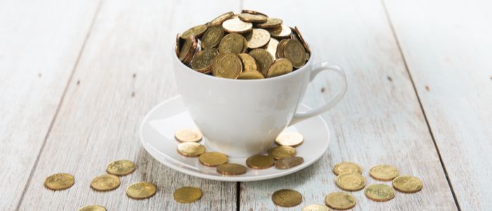A cup and saucer filled with coins, with coins spilling over