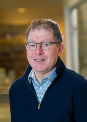 Photo of Professor Andrew Tobin wearing a shirt and navy jumper against an abstract background in his lab