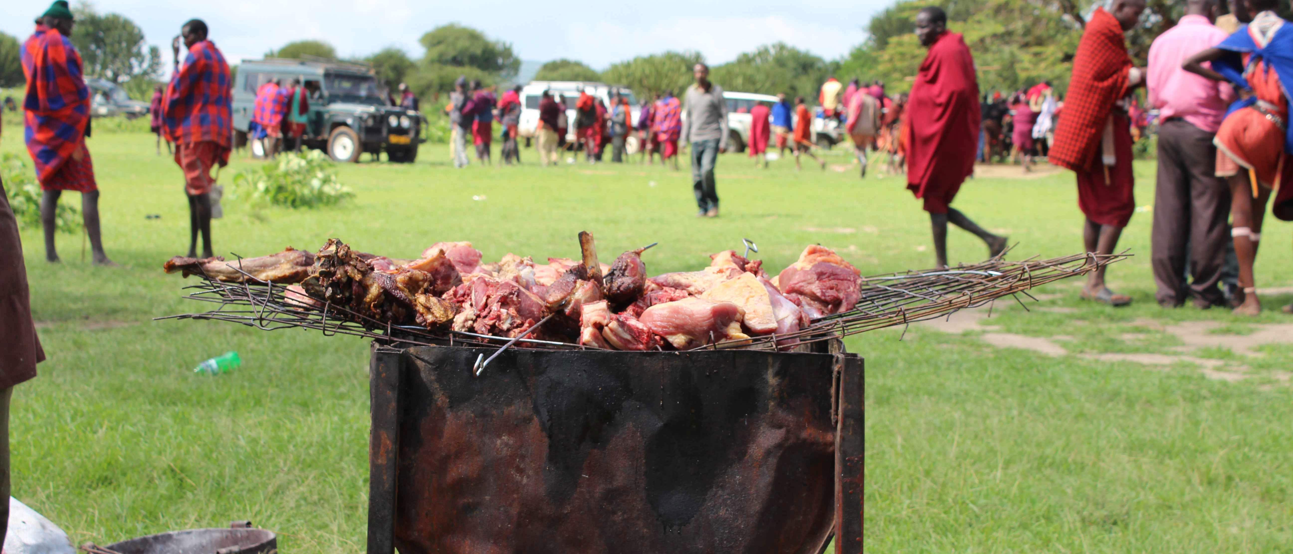 Meat cooking on an open grill with people in the background