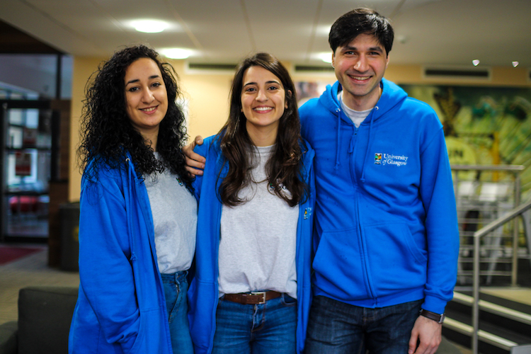 Three Living Support Assistants wearing blue hoodies and grey t-shirts standing together smiling
