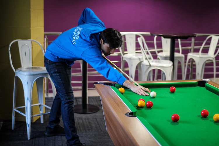 A male Living Support Assistant in a blue hoody playing pool