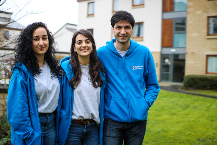 Three Residence Assistants wearing blue hoodies in a grassy courtyard at Queen Margaret Residences