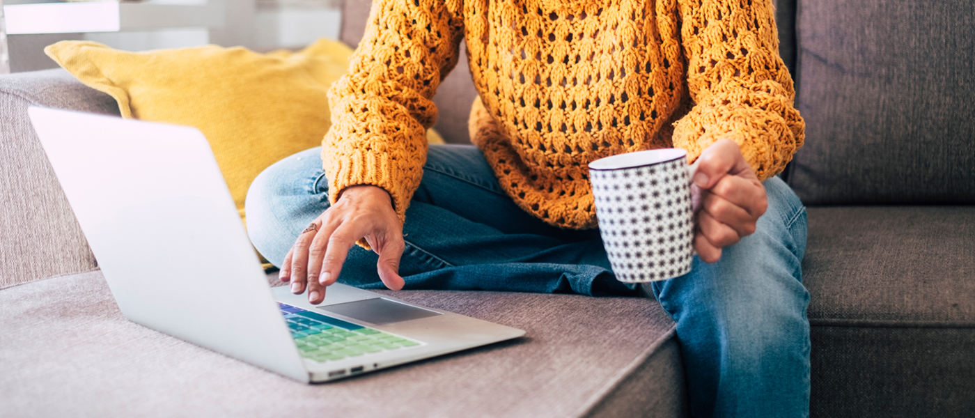 Photo of person in yellow jumper using laptop and drinking coffee