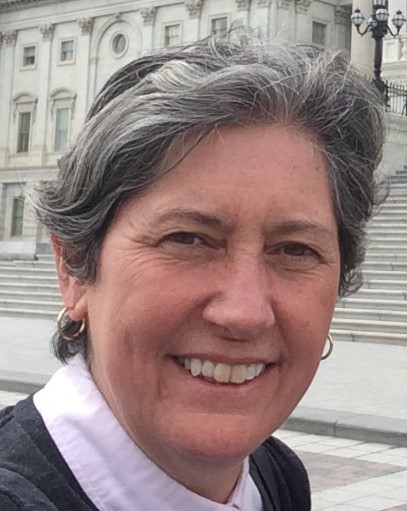 Close up of Sue John showing just head and shoulders. It is taken outside, in front of a building with steps in the background.