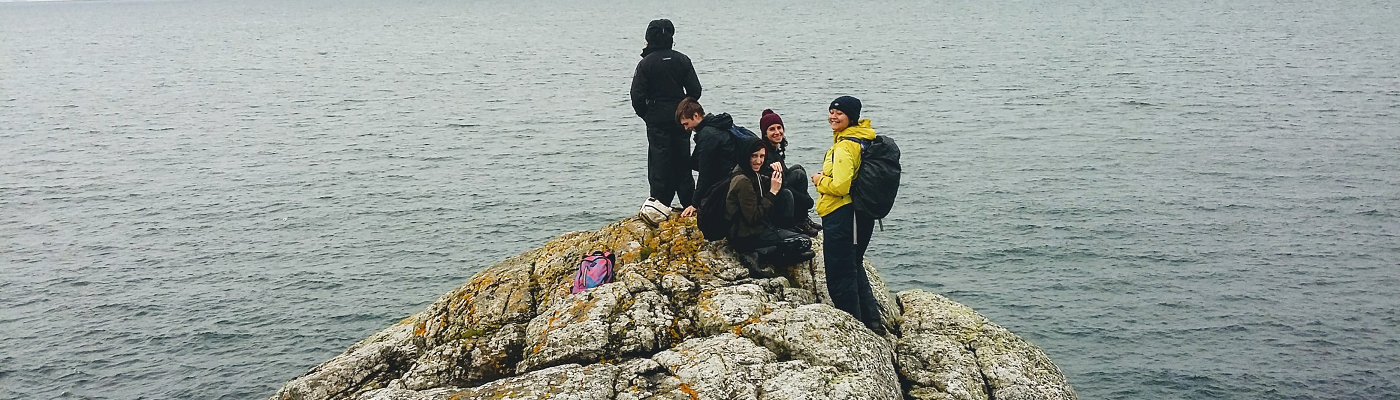 Students on the rocks by the sea - 1400x400